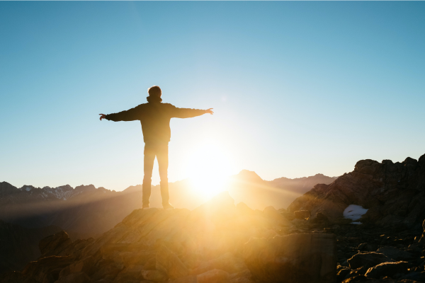 Man with outstretched arms on mountaintop facing into bright sunshine post-divorce